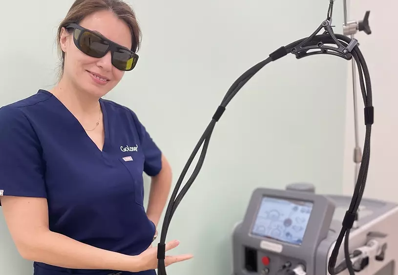 A GoLaser technician wearing safety glasses and blue GoLaser scrubs standing next to a laser hair removal machine