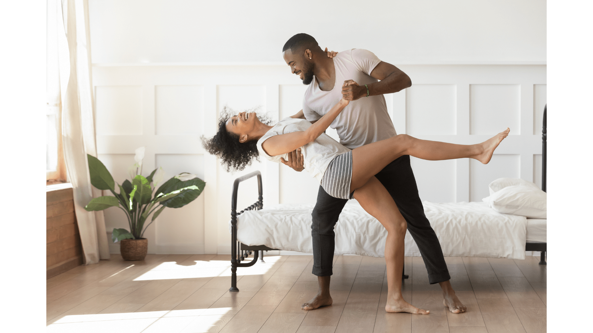 A couple dancing together in their bedroom next to the bed
