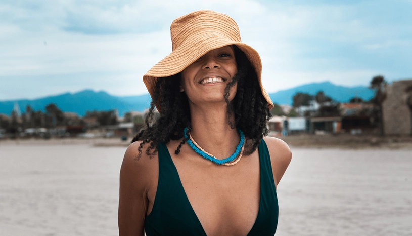 Close up of a woman wearing a hat smiling as she walks on sand