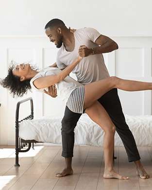 A couple dancing together in their bedroom next to the bed